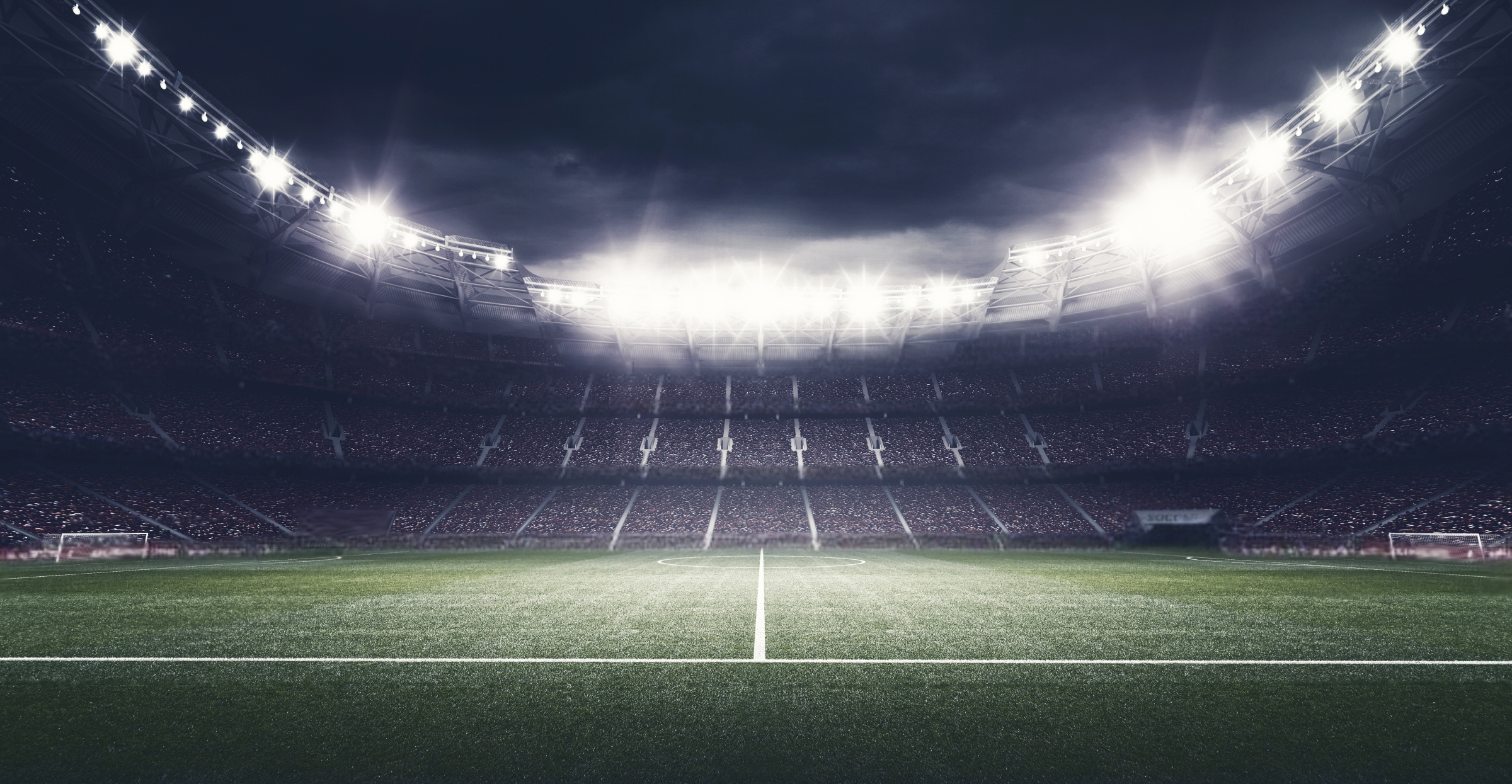 Looking up from the pitch of a large, empty football stadium at night.