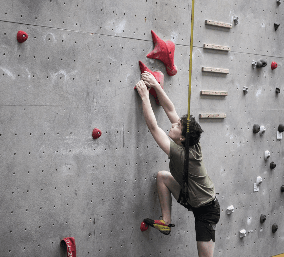 An amateur climber attempting a new personal best at an indoor climbing wall.