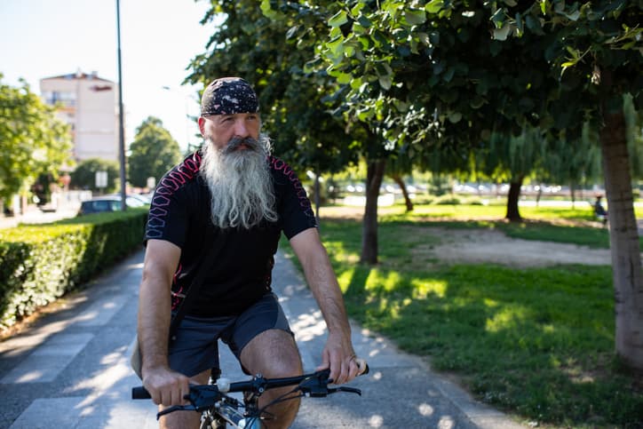 A Scorado profile picture of an older man with a long white beard casually cycling along a city street.