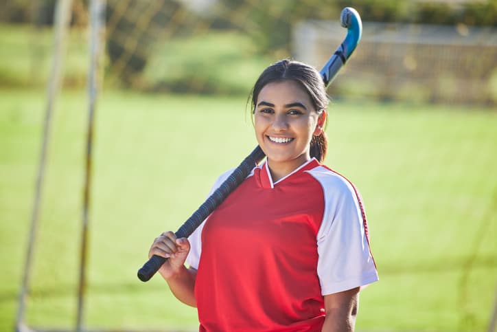 A Scorado profile picture of a young a Asian girl wearing a sports jersey holding her hockey stick in the air.